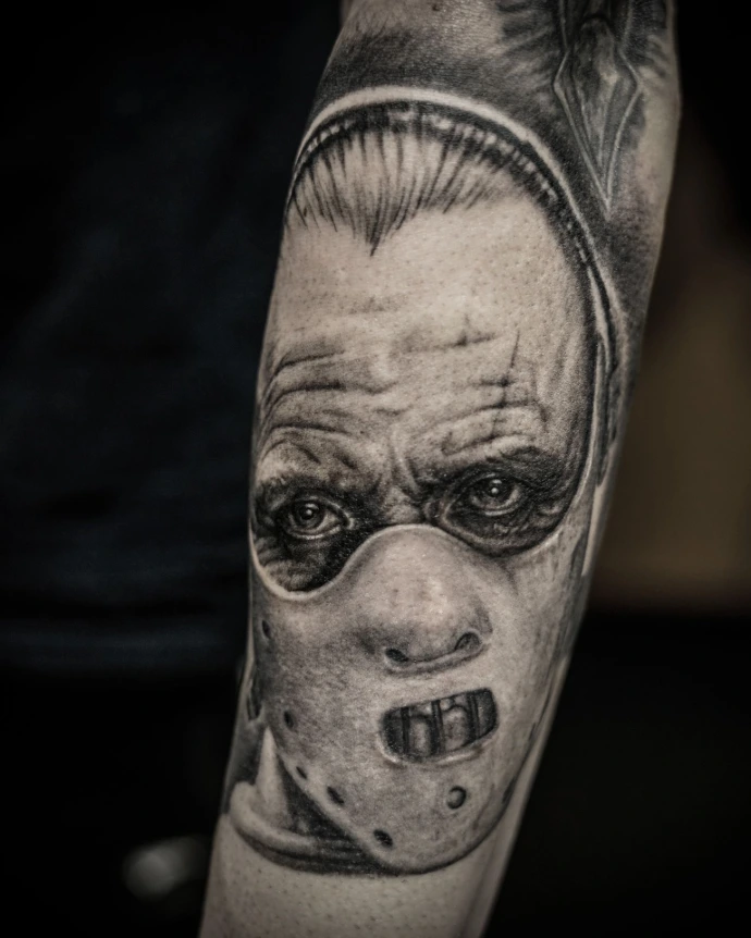 Black and grey realism tattoo of Hannibal Lecter from Silence of the Lambs, featuring the iconic muzzle mask and intense eye contact.