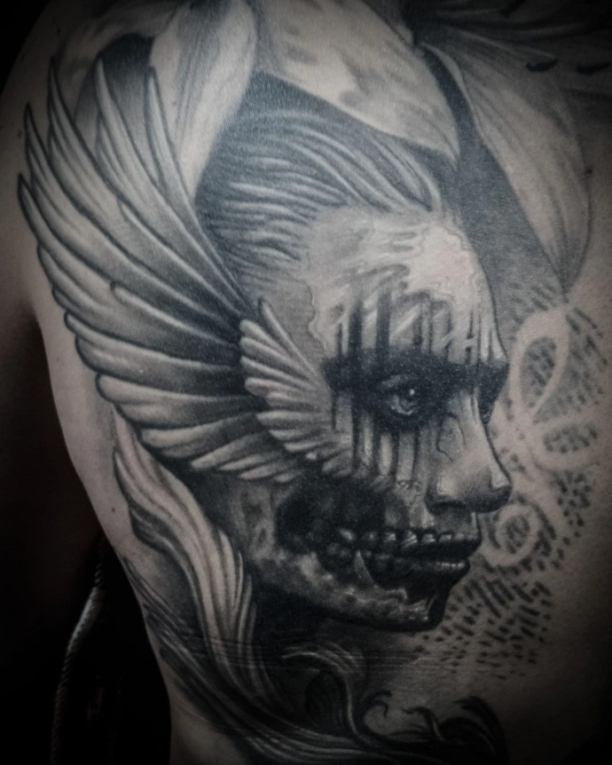 Dark surrealism Valkyrie tattoo showing a half-living, half-skeletal face with angel wings and gothic details.