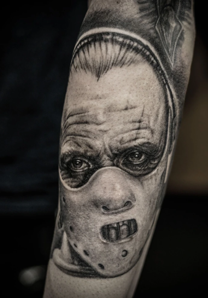Black and grey realism tattoo of Hannibal Lecter from Silence of the Lambs, featuring the iconic muzzle mask and intense eye contact.