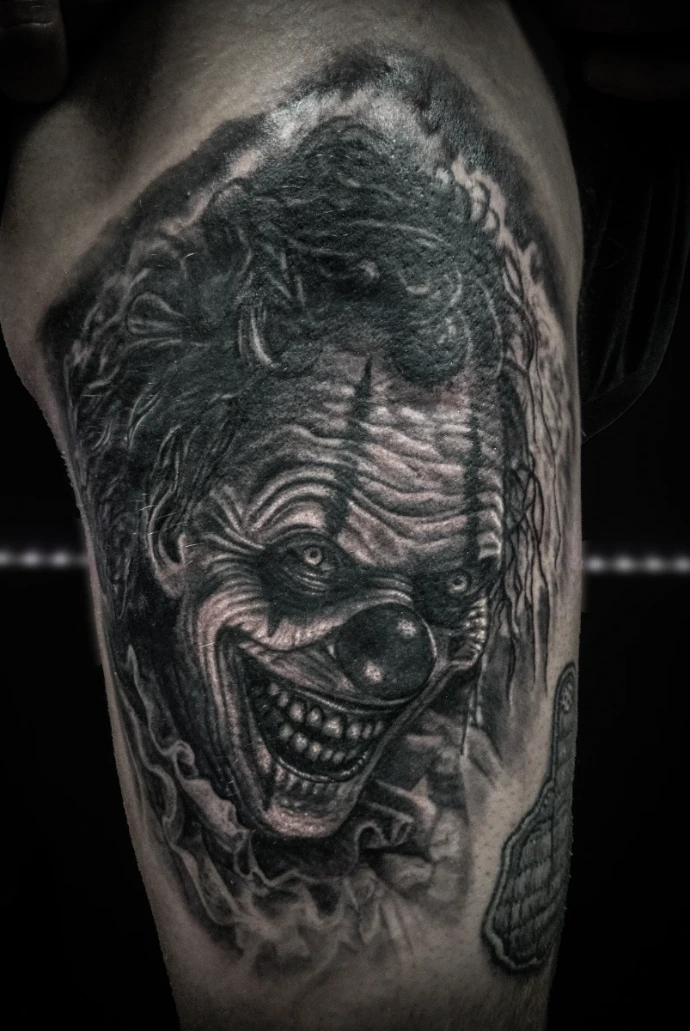 Black and grey realism tattoo of Pennywise the Dancing Clown from the movie IT, featuring detailed skin texture, sharp teeth, and sinister expression.